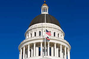 The California State Capitol dome and United States flag against a deep blue sky.