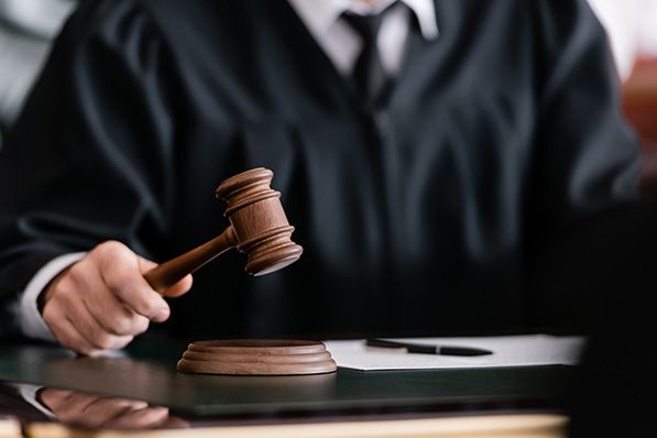 A judge in a black robe holds a gavel above a sound block.