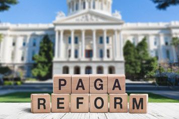 Wooden blocks spell PAGA REFORM in front of a blurred capitol building.