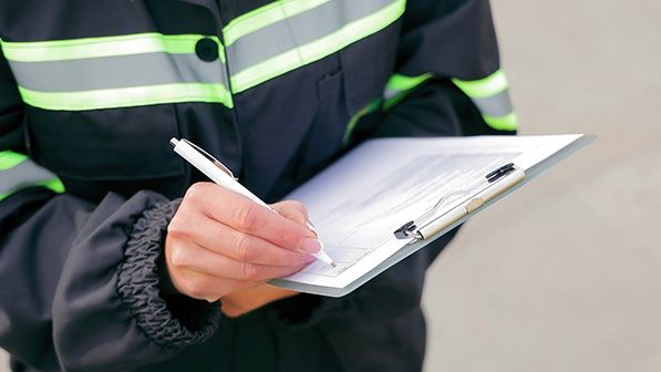 A worker in a reflective jacket writes on a clipboard.