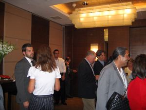 Attendees mingle in a warmly lit conference room beneath rectangular ceiling lights.