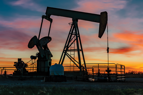 An oil pumpjack silhouetted against a pink and orange sunset.