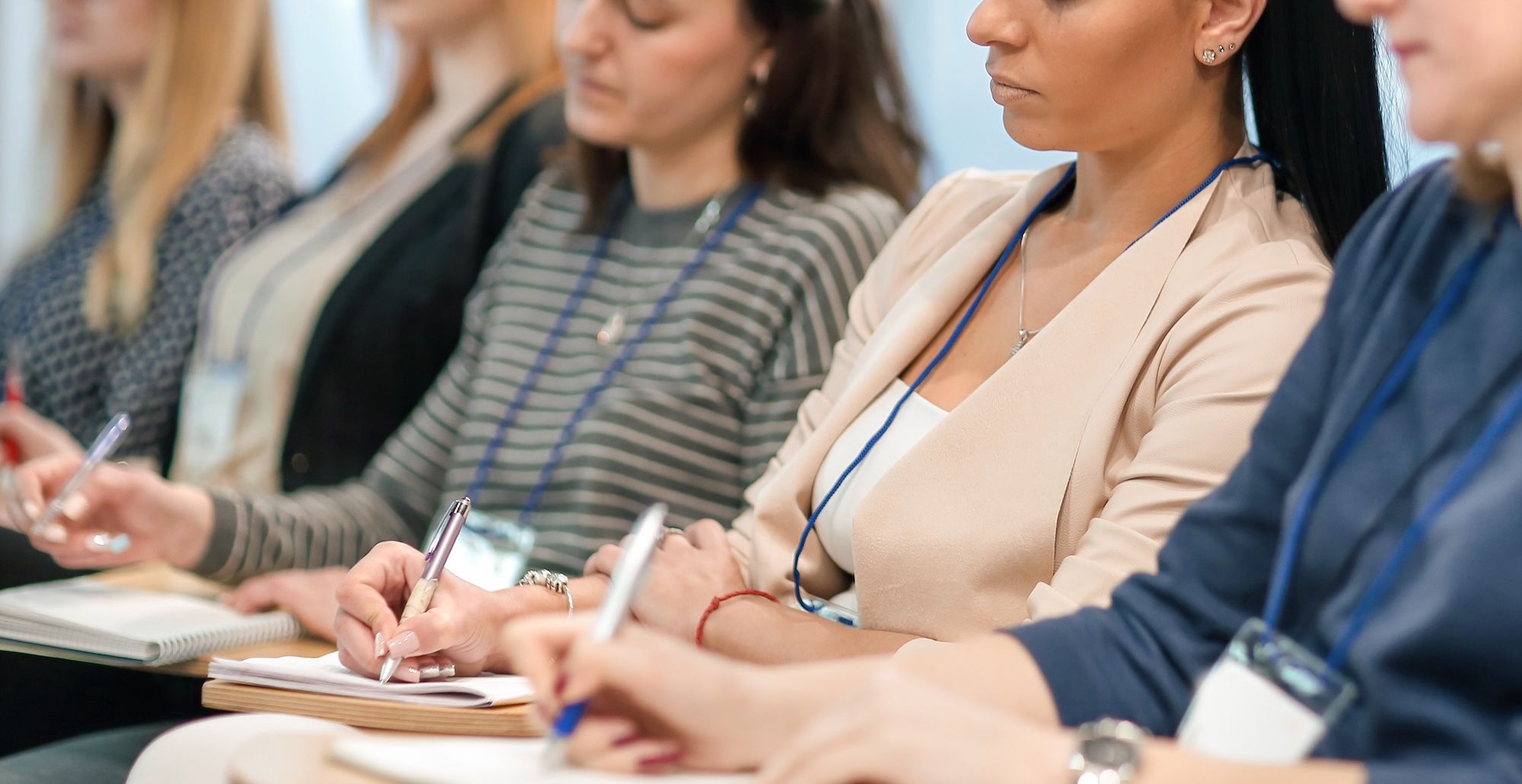 Seated attendees wearing lanyards take notes in notebooks.
