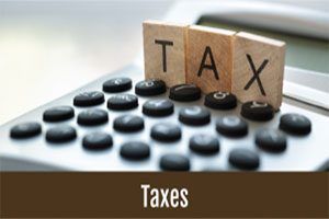 Wooden TAX blocks on a calculator above a brown banner labeled Taxes.