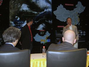 A presenter speaks beside a map of China as attendees sit facing him.