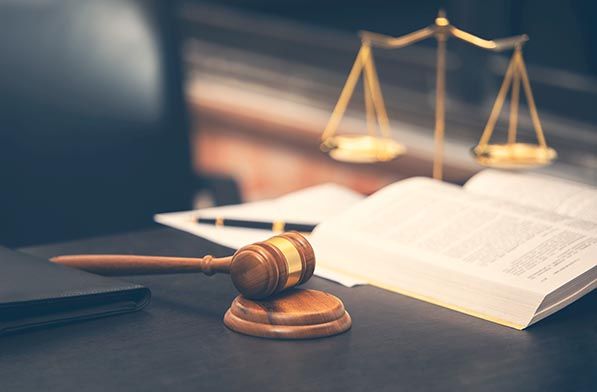 A wooden gavel rests beside an open law book with gold balance scales behind it.