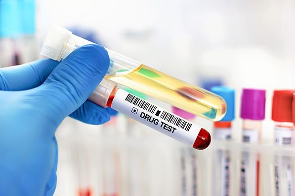 A blue-gloved hand holds sample tubes, including one labeled DRUG TEST.