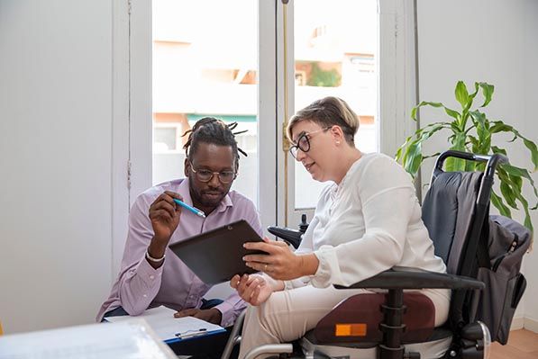 Two coworkers review a tablet together, one seated in a powered wheelchair.