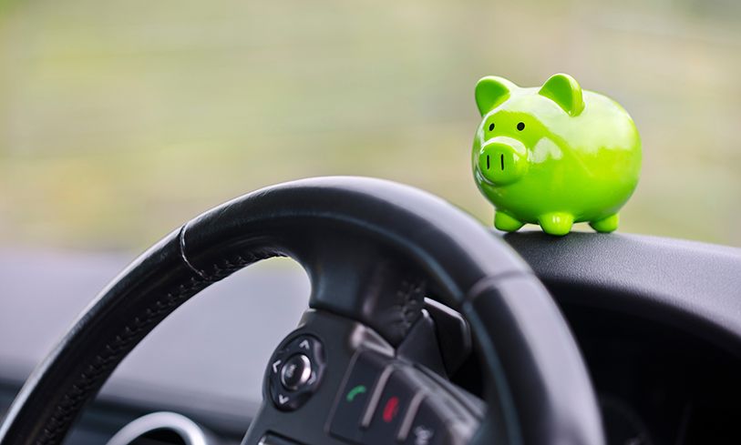 A green piggy bank sits on a car dashboard above the steering wheel.