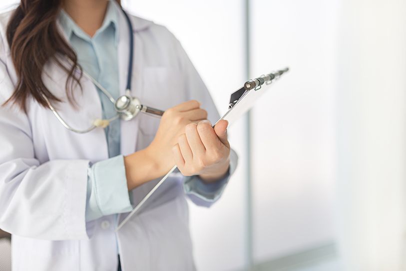 A healthcare professional in a white coat with a stethoscope holds a clipboard.