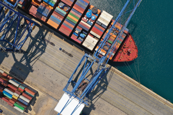 Overhead view of a container ship docked beside blue cargo cranes and stacked containers.