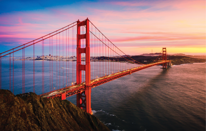 The Golden Gate Bridge crosses the bay beneath a pink and orange sunset.