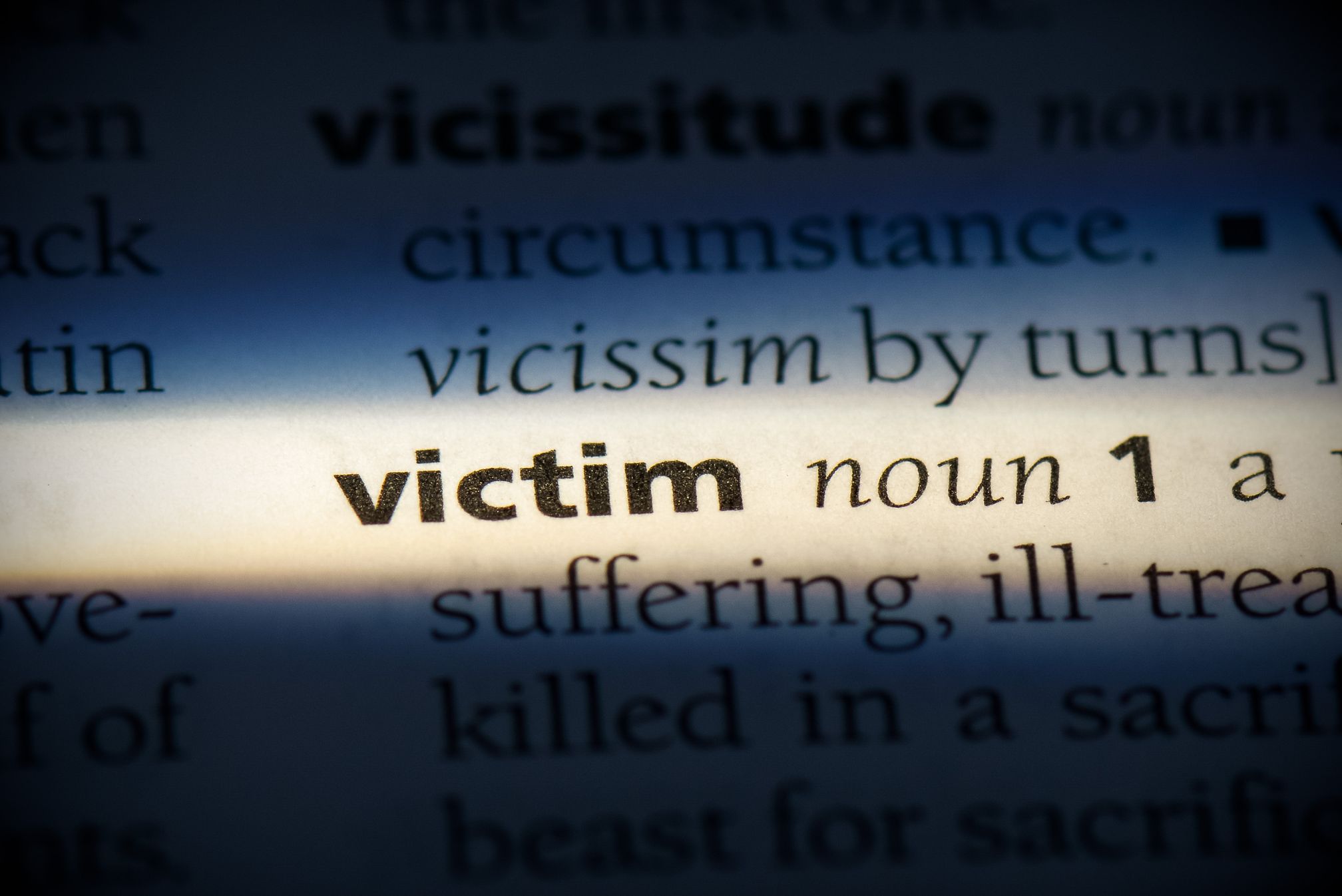 A dictionary entry for victim is illuminated while the surrounding text falls into shadow.