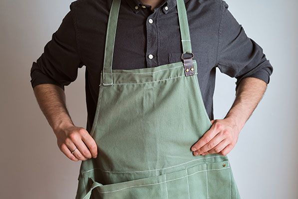 A person wearing a green apron stands with both hands on their hips.