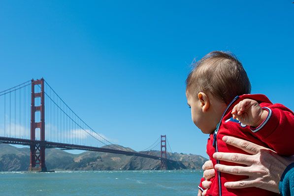 A baby held by an adult looks out at the Golden Gate Bridge.