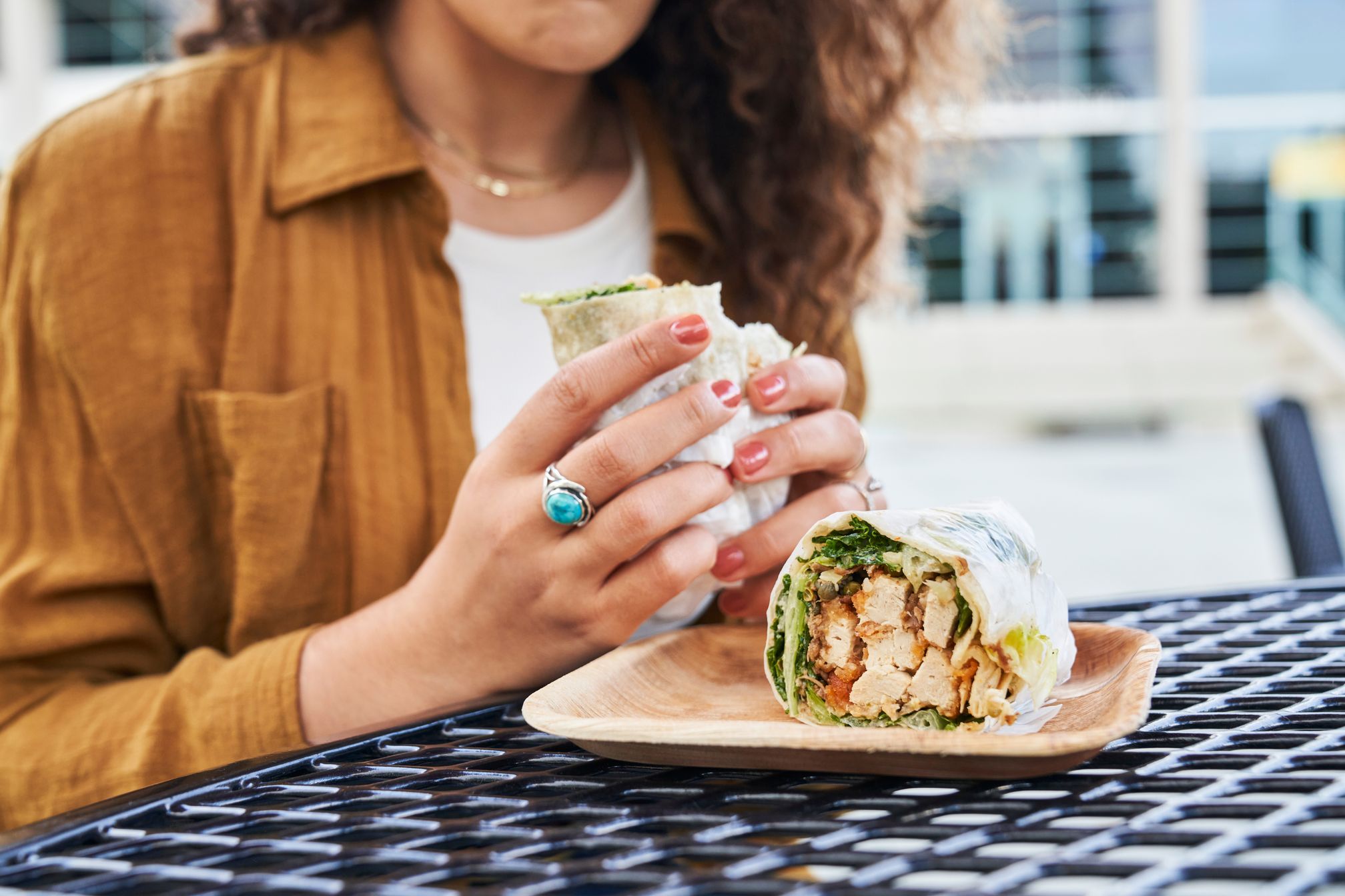A person holds a wrap sandwich at an outdoor table with another half on a plate.