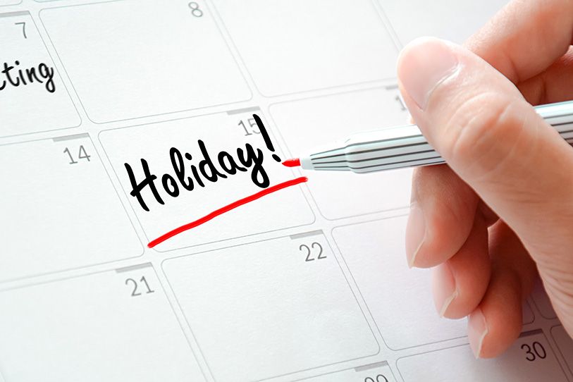 Hand marking "Holiday!" on a calendar with a red pen.