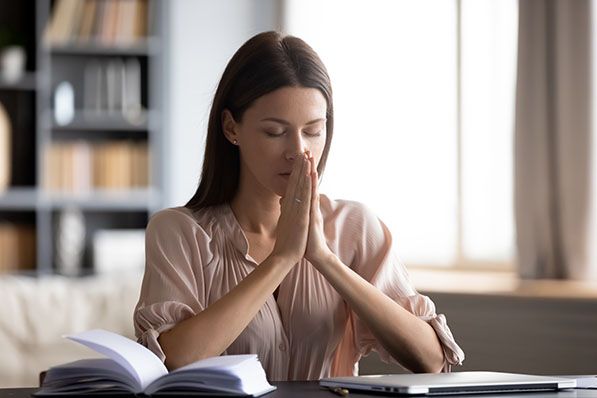 A woman with closed eyes and hands clasped together, meditating or praying.