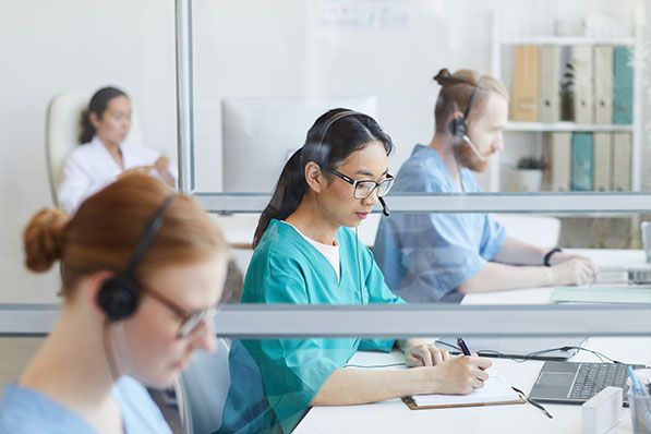 Healthcare workers wearing headsets work at computers in a shared office.