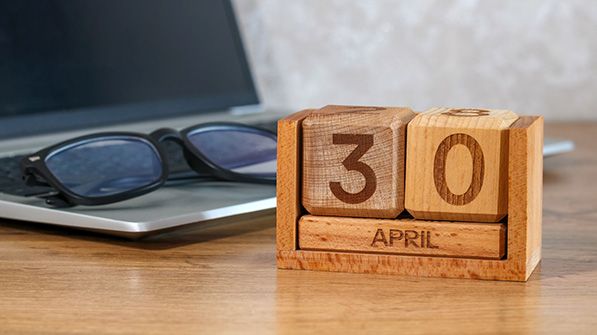 Wooden block calendar displaying April 30 beside glasses and a laptop.