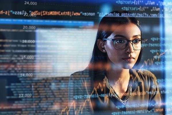 A woman wearing glasses is seen behind layers of computer code and numeric displays.
