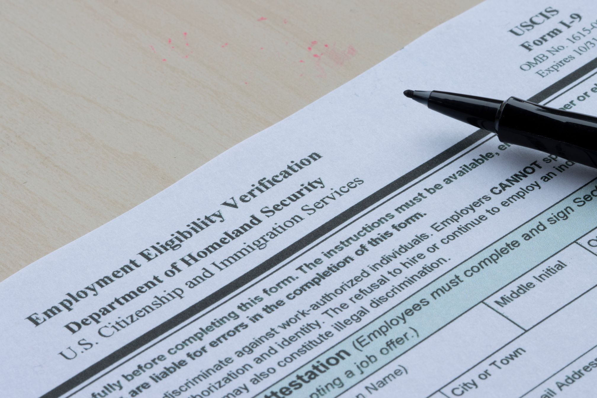 A pen rests on an Employment Eligibility Verification form from U.S. Citizenship and Immigration Services.