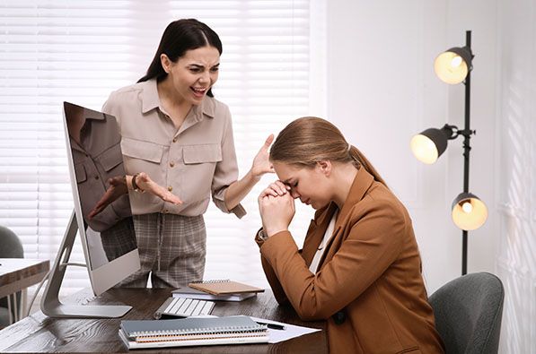 A standing woman gestures beside a seated coworker leaning forward with her hands near her face.