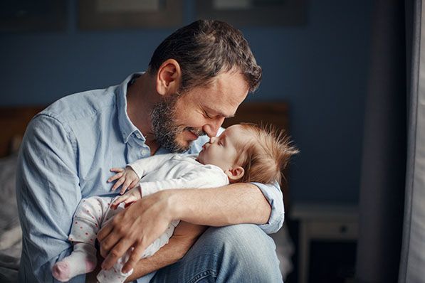 A man cradles a baby and leans close to the baby's face.