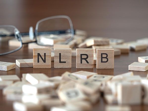 Wooden letter tiles spell NLRB among scattered tiles beside eyeglasses.