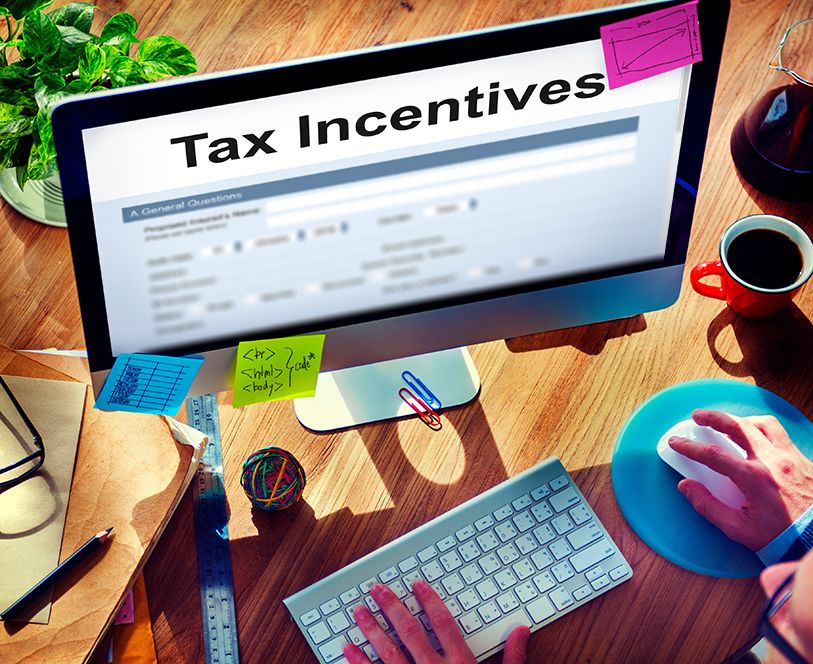 A desktop computer displays Tax Incentives above a form on a colorful office desk.