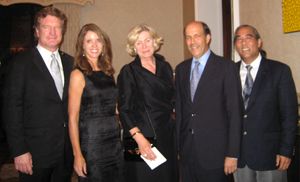 Five people in formal business attire pose together indoors.