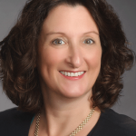 Portrait of a smiling woman with shoulder-length curly dark hair wearing a black top and necklace.