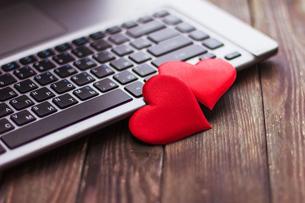 Two red hearts rest beside a laptop keyboard on a wooden desk.