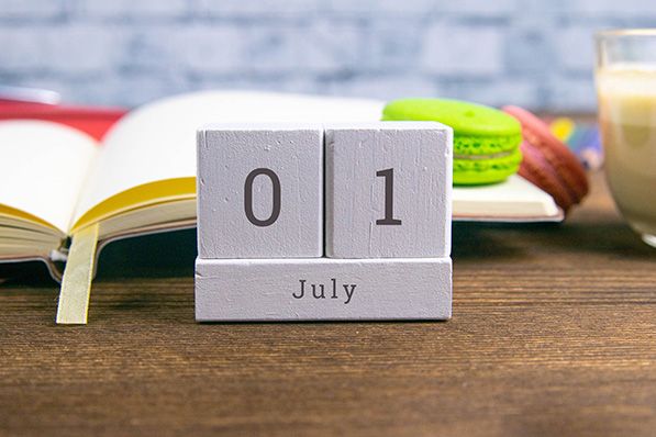 Gray wooden calendar blocks display July 1 on a table beside an open book.