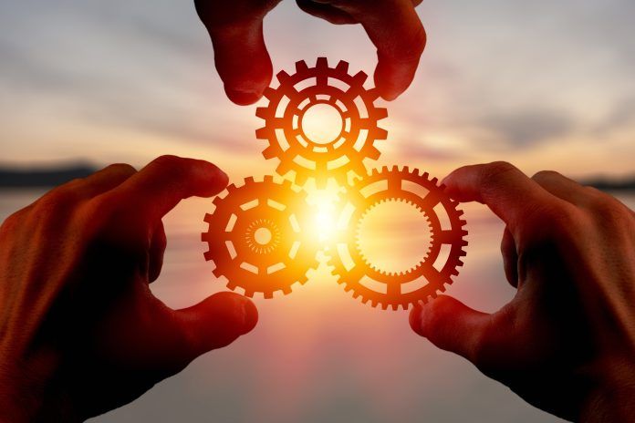 Hands hold three interlocking gears against warm sunlight.