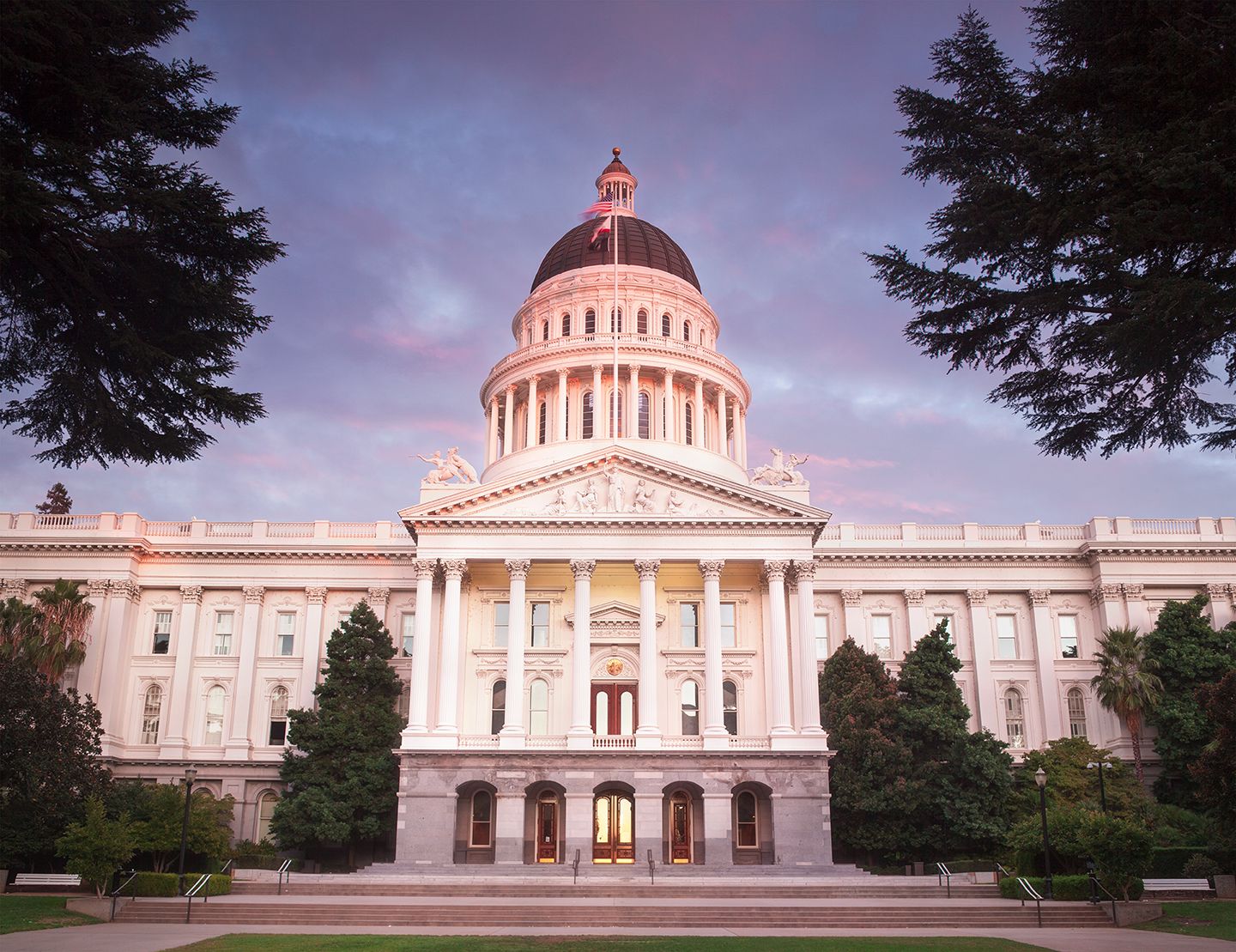 The California State Capitol framed by trees beneath a purple evening sky.