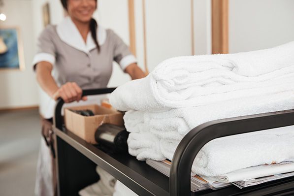A hotel housekeeper pushes a cart stacked with folded white towels.