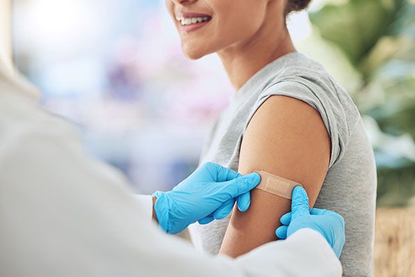 Blue-gloved hands place a small bandage on a person's upper arm.