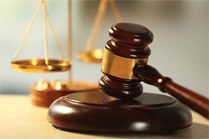 A wooden judge's gavel and sound block with a brass balance scale behind them.