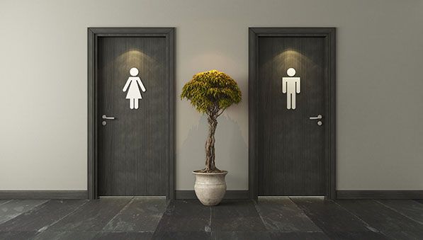 Two restroom doors marked with woman and man symbols, separated by a potted tree.