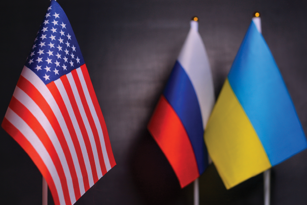 U.S., Russian and Ukrainian flags displayed on poles against a dark background.