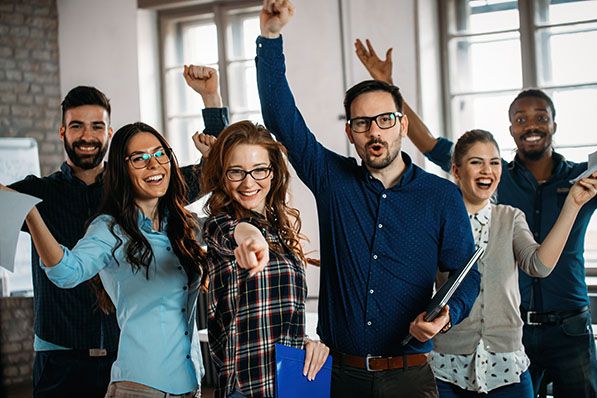 A group of office coworkers smile and raise their arms together.