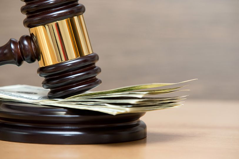 A wooden gavel hovers above a stack of dollar bills on its block.