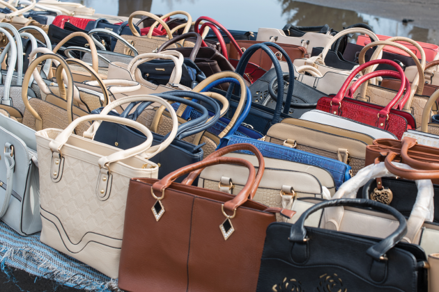 Rows of handbags in assorted colors and styles displayed on a table.