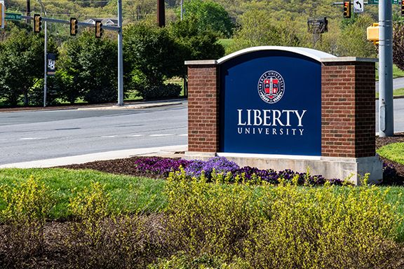 Liberty University entrance sign beside a road and landscaped flowers.