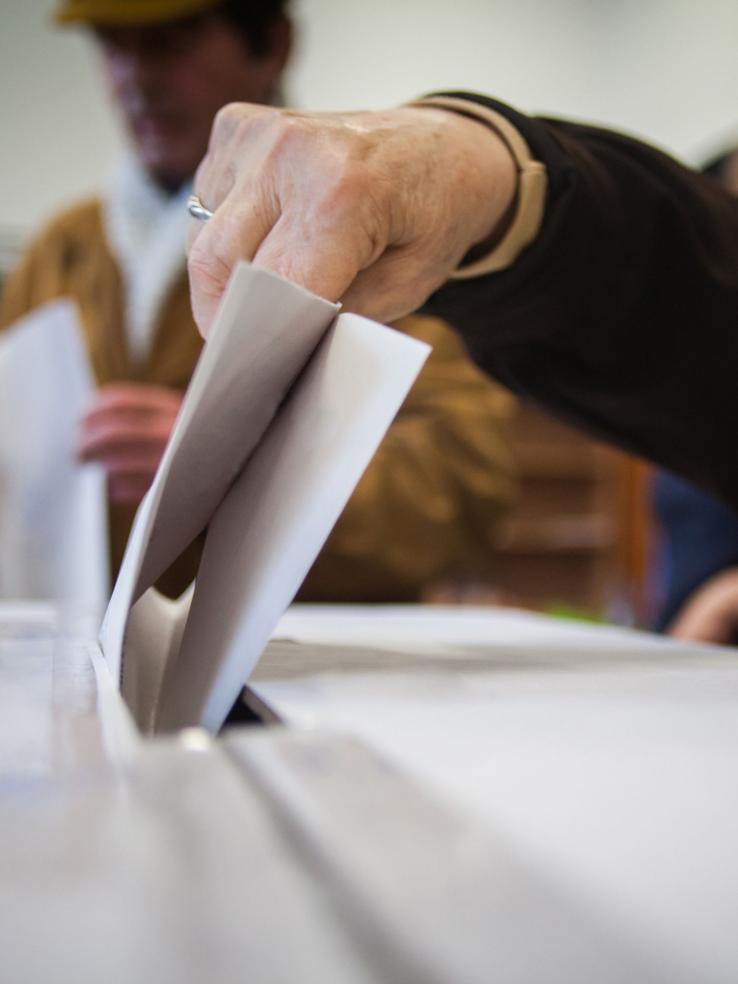 A hand places a folded ballot into a ballot box.