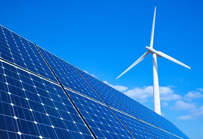 Blue solar panels and a white wind turbine beneath a clear sky.