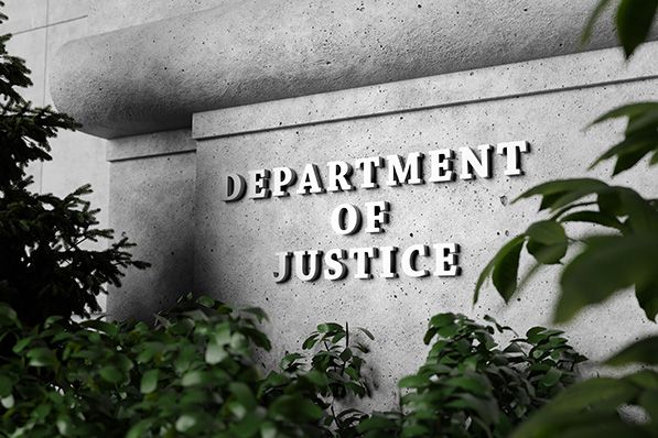 Department of Justice lettering carved into a stone wall surrounded by foliage.