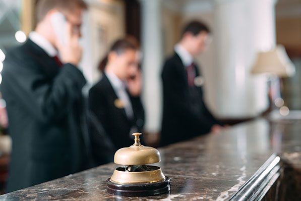 A brass bell on a hotel reception desk with uniformed staff out of focus in the background.
