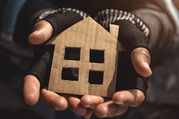Hands in fingerless gloves cup a small cardboard house.